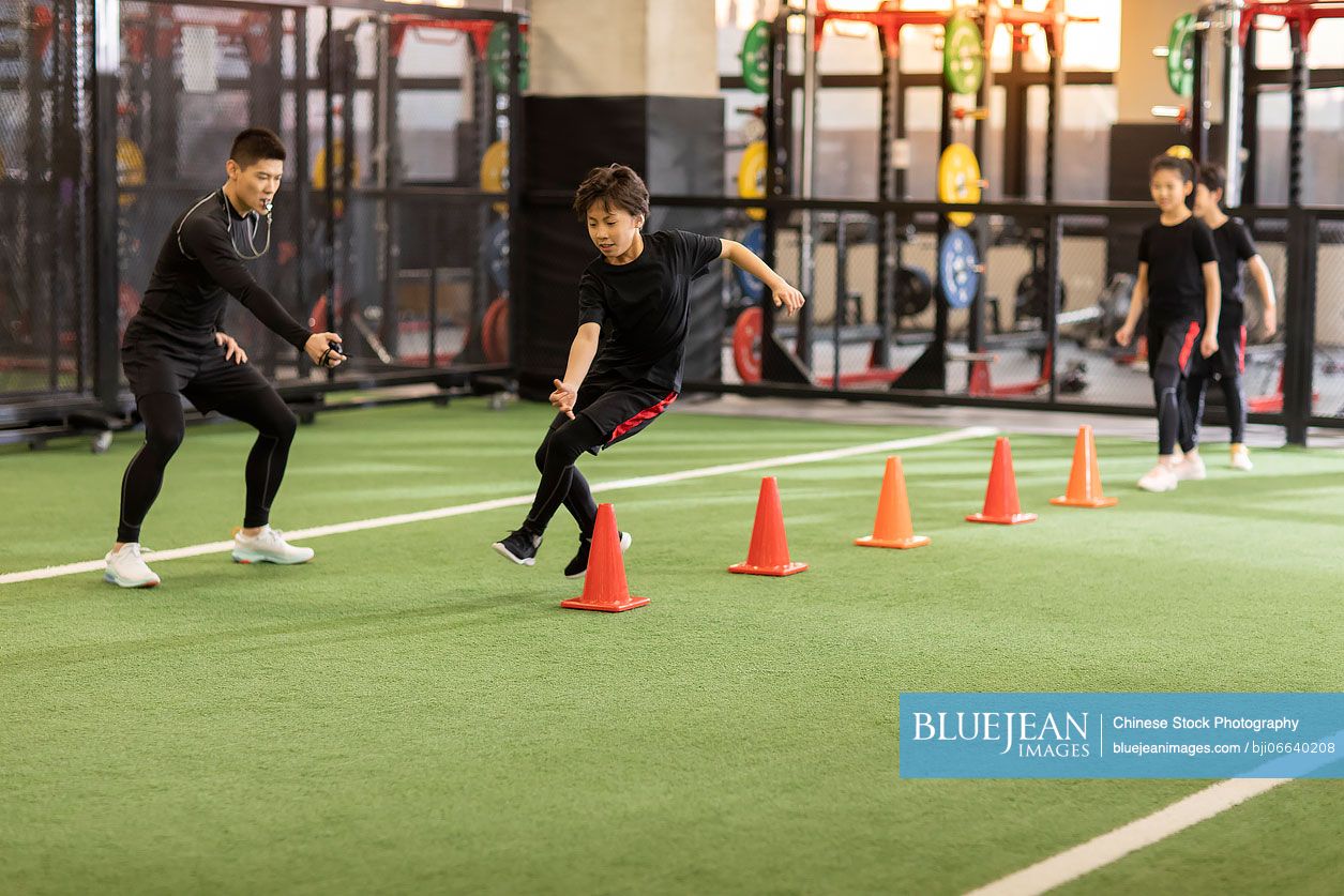 Active Chinese children having exercise class with their coach in gym