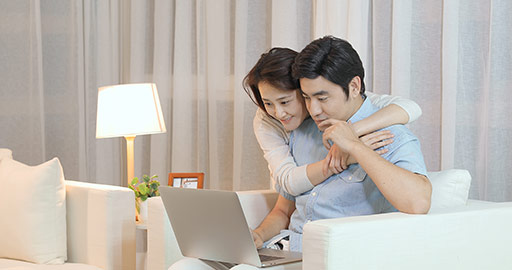 Happy young Chinese couple using laptop in living room,4K