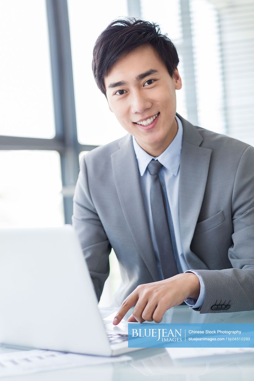 Young Chinese businessman using laptop in office