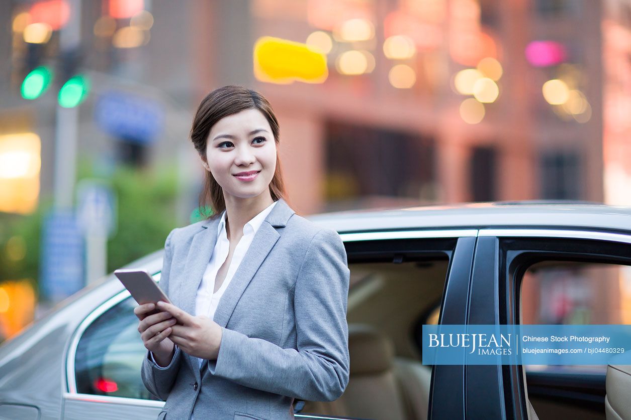 Chinese businesswoman standing next to the car with smart phone