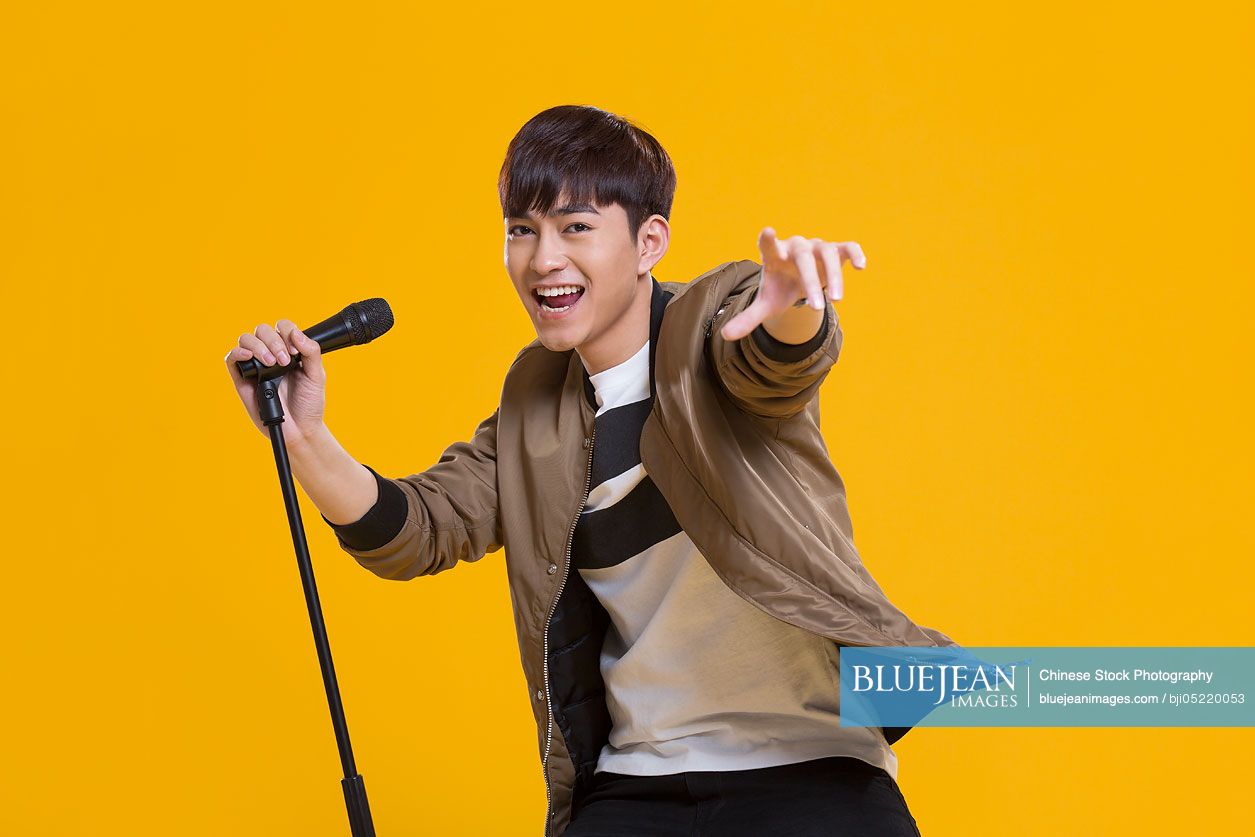 Cheerful young Chinese man singing with microphone