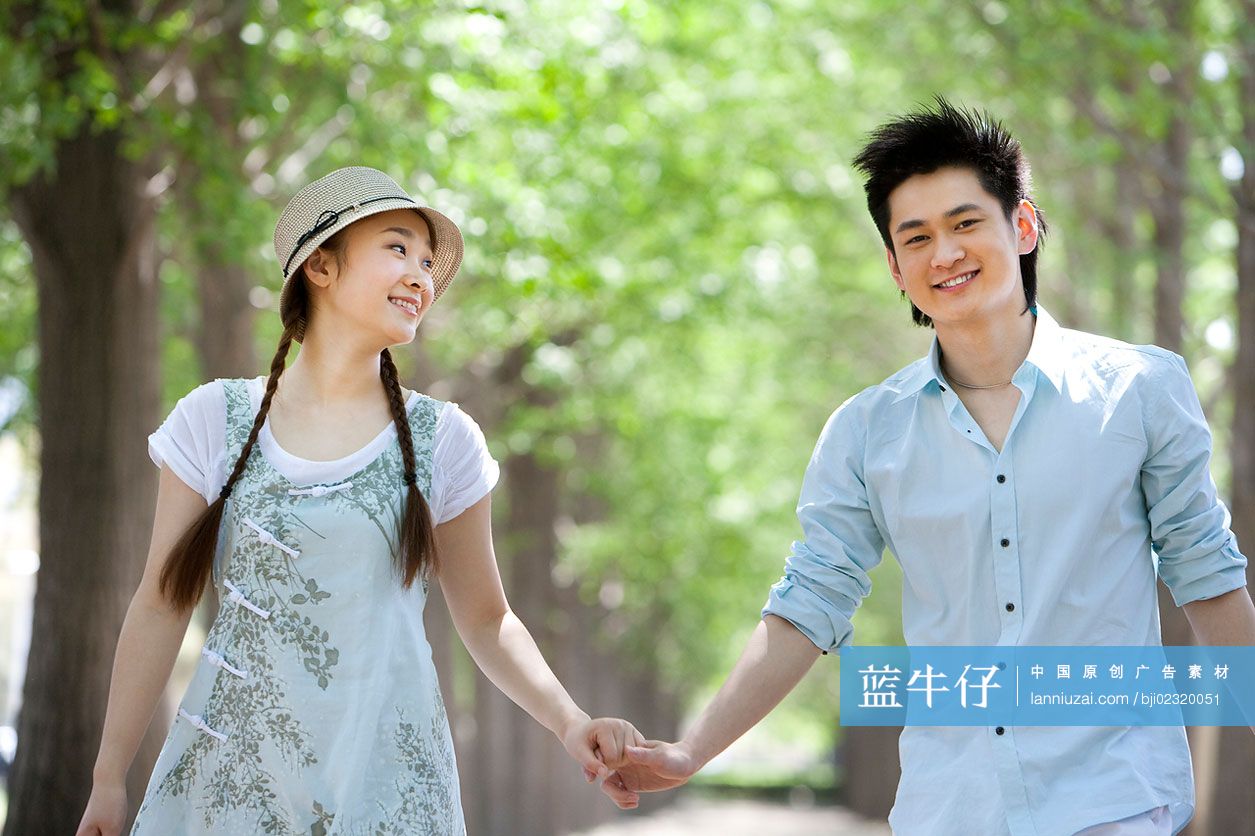 快乐的年轻情侣手牵手在草地上散步-蓝牛仔影像-中国原创广告影像素材