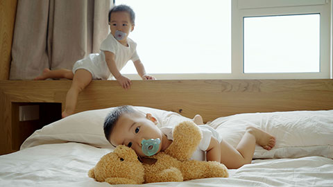 Two twin babies with pacifiers playing on the bed.