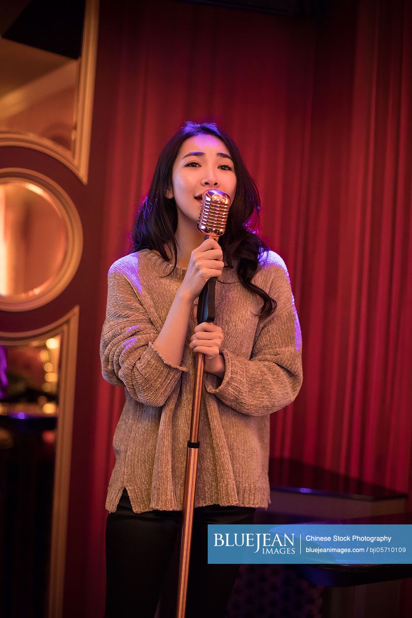 Beautiful young Chinese woman singing karaoke in nightclub