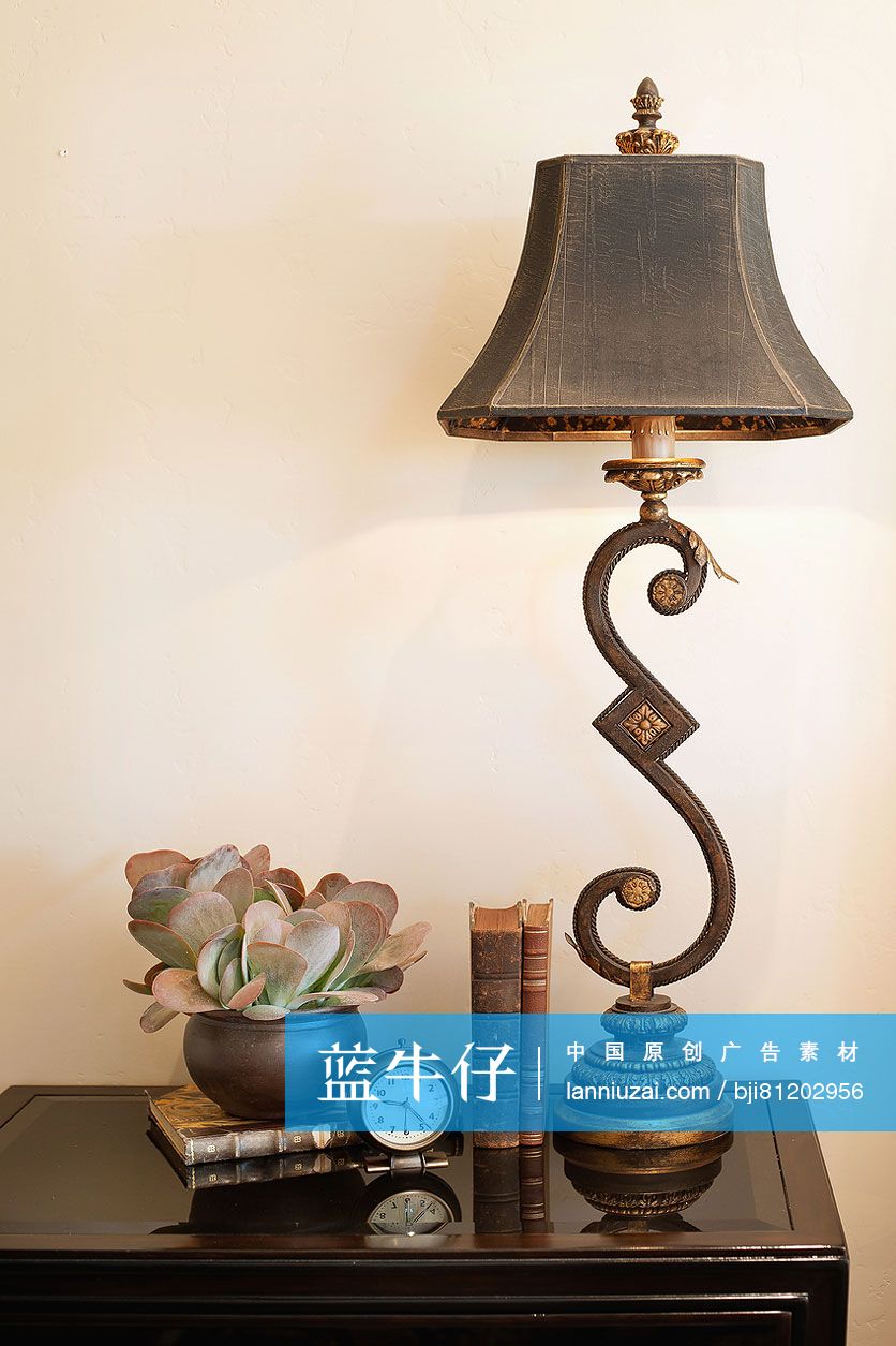 Lamp with books; clock and vase on console table against wall at home