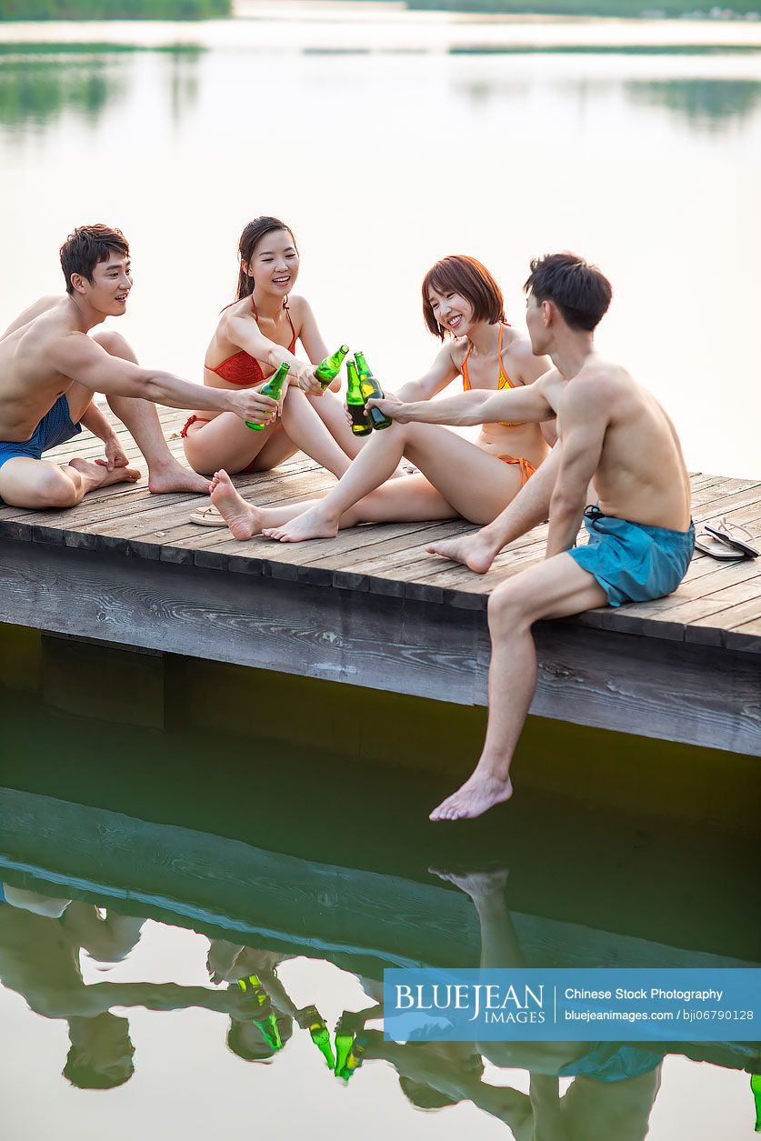 Happy young Chinese friends toasting with beer and relaxing on a jetty