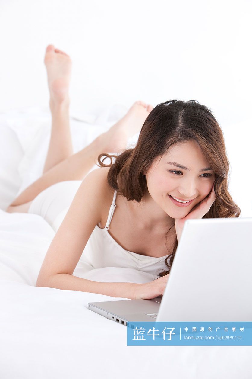 床上趴着用笔记本电脑的年轻女性