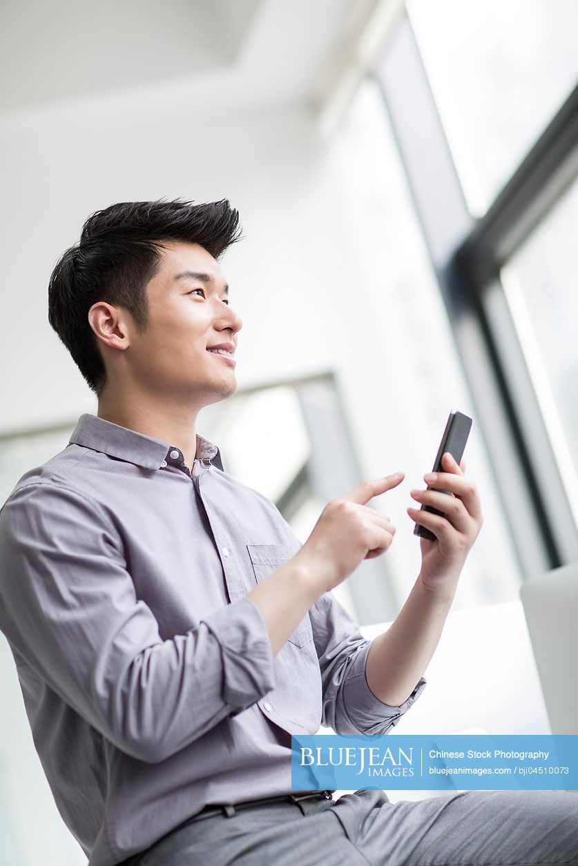 Young Chinese businessman using smart phone in office