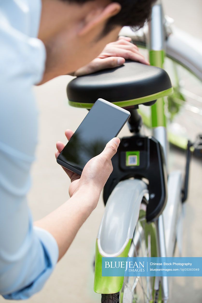 Young chinese man scanning a qr code to unlock a share bike high res