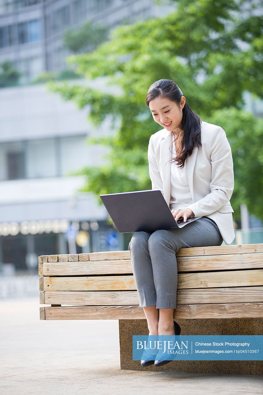 Young Chinese businesswoman working with laptop outdoors