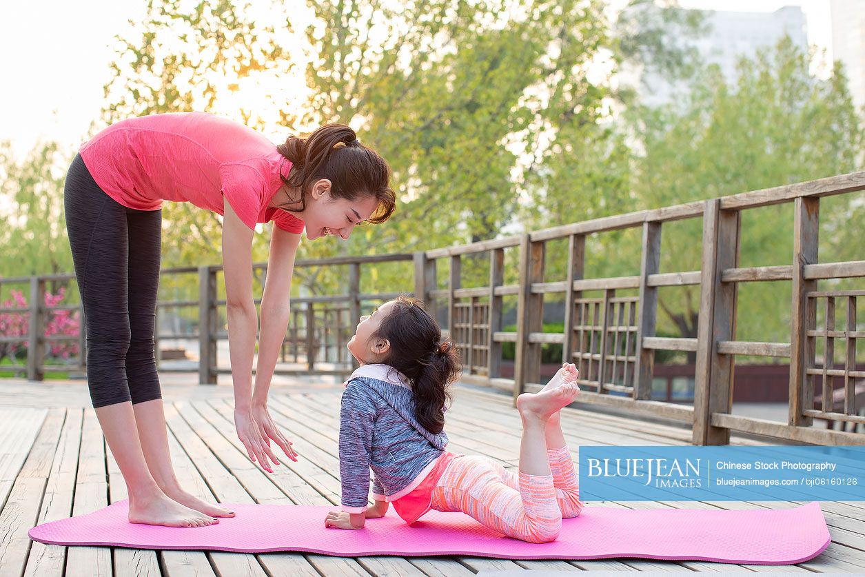 Happy Chinese mother and daughter doing yoga outdoors