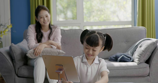 Little girl taking an online class with her mom keeping her company
