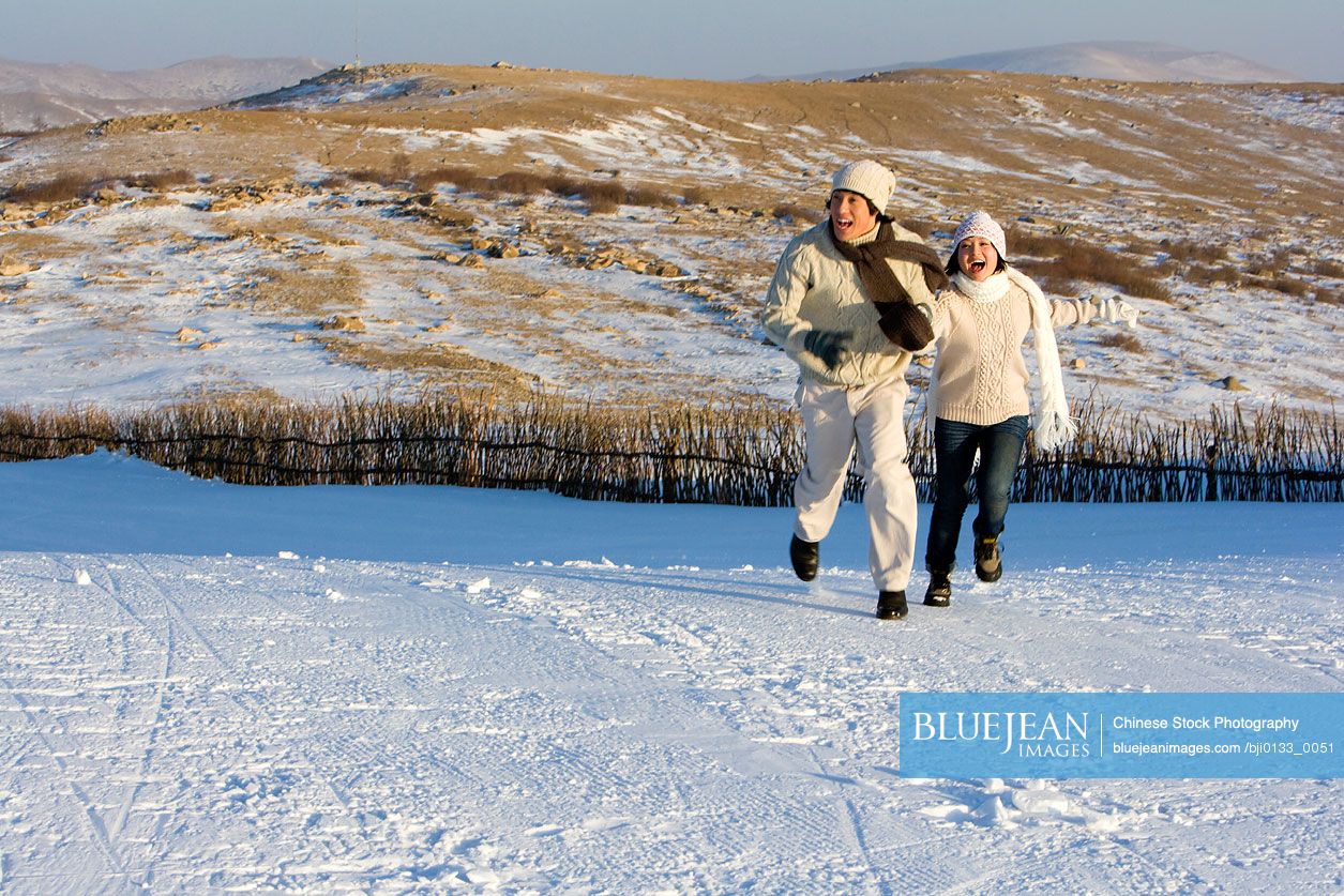 Young Chinese man and young Chinese woman running in the snow