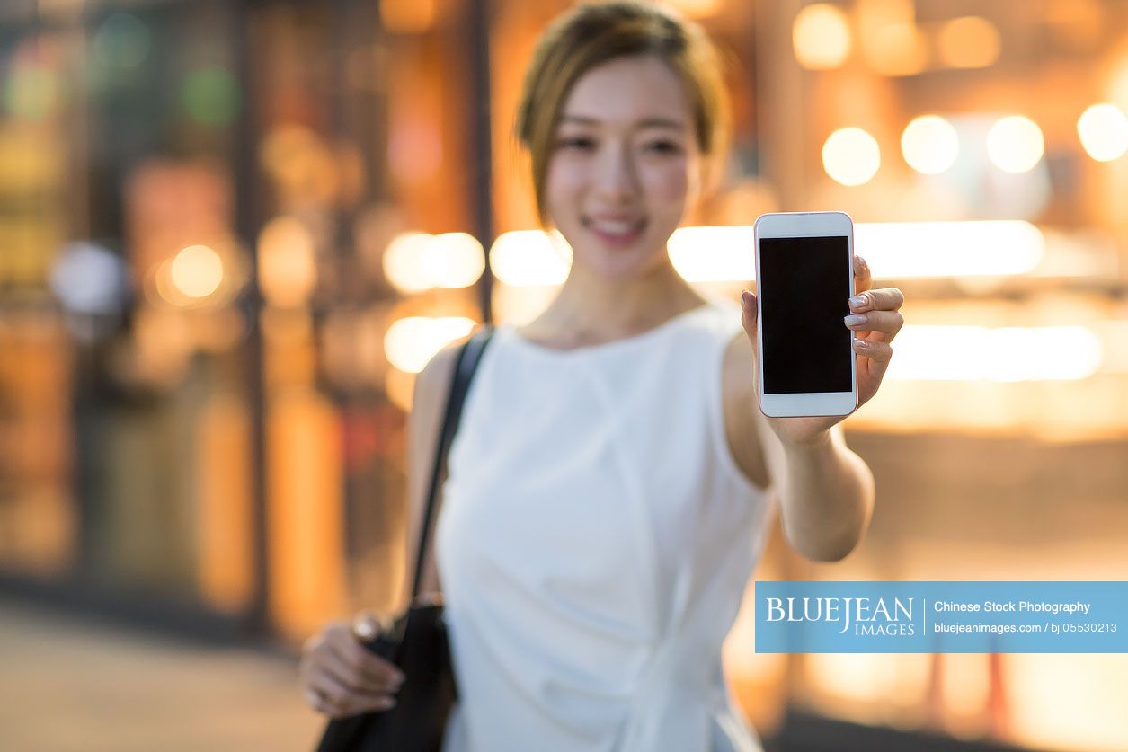 Cheerful young Chinese woman showing a smart phone
