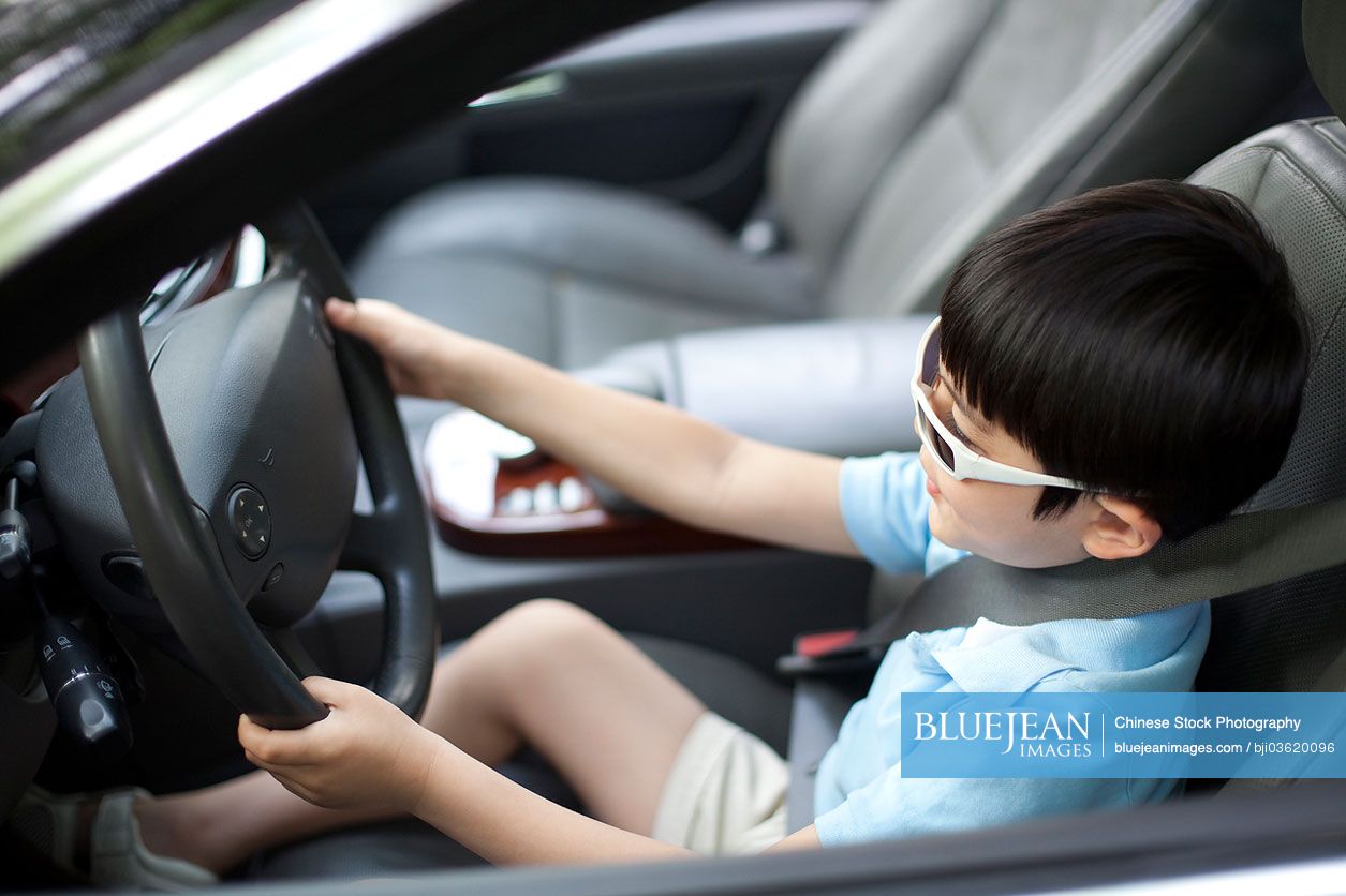 Cute young Chinese boy pretending to drive car