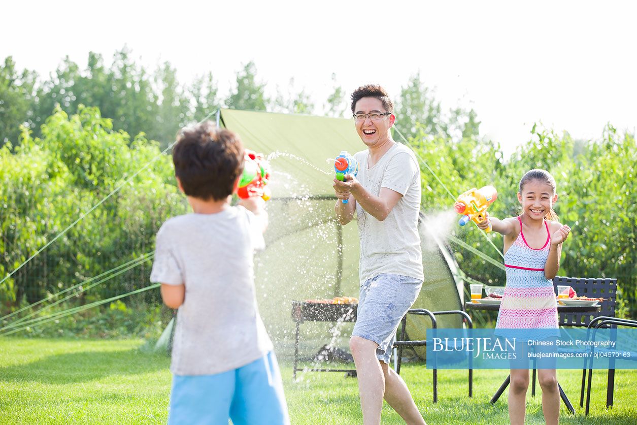 Happy Chinese father and children playing squirt guns