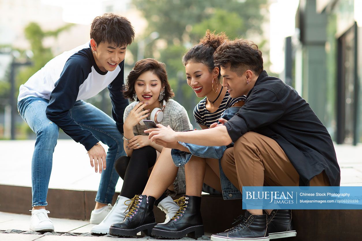 Happy young Chinese friends using smartphone outdoors