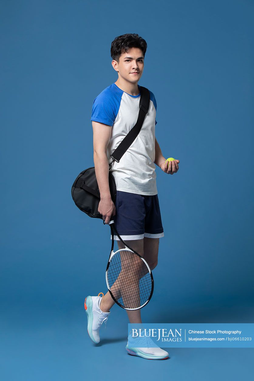 Studio shot of young Chinese man playing tennis