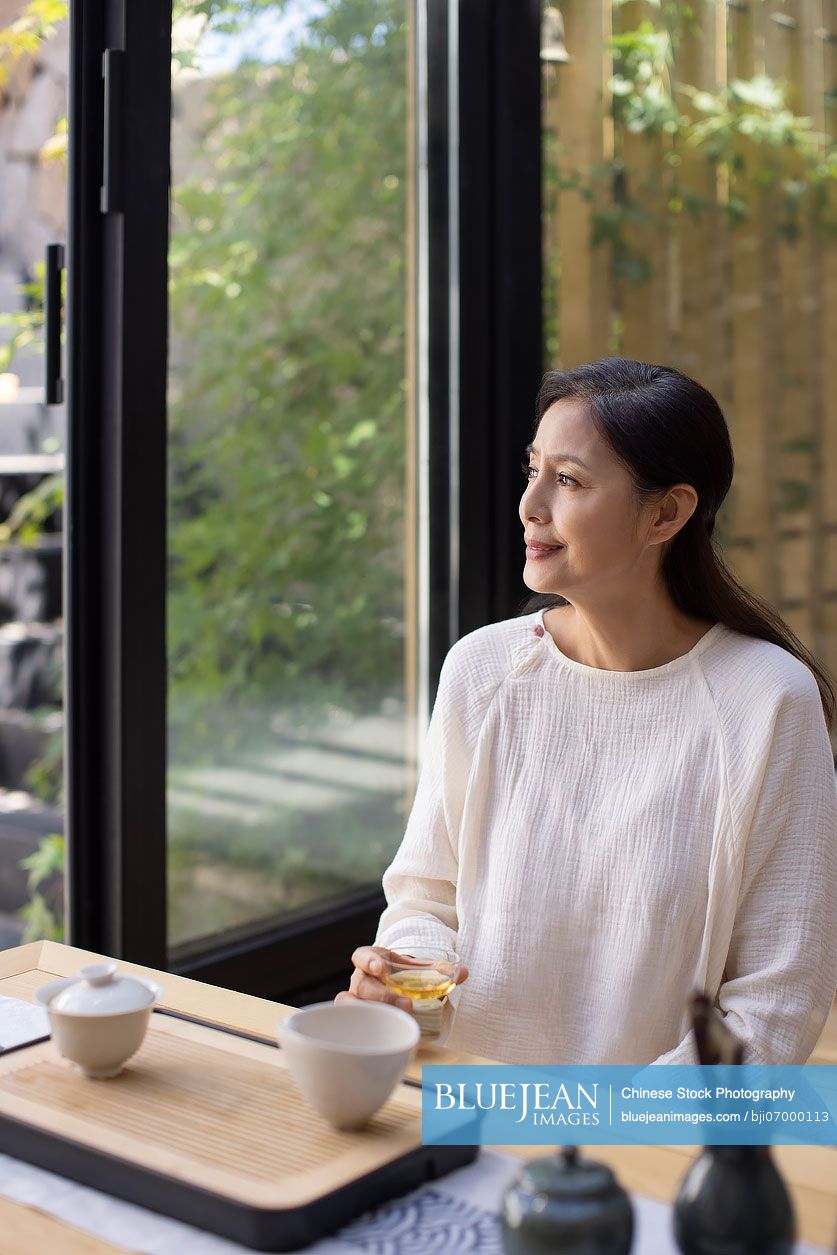 Elegant mature Chinese woman drinking tea in tea room