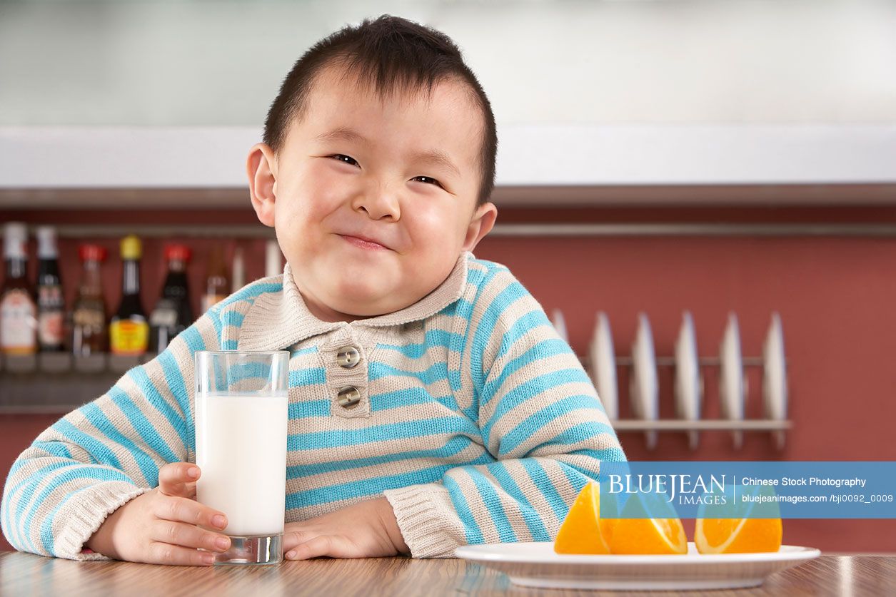Young Chinese boy drinking milk and eating oranges