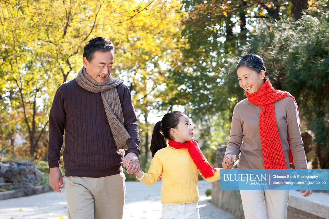 Senior Chinese couple with granddaughter strolling through the park in autumn