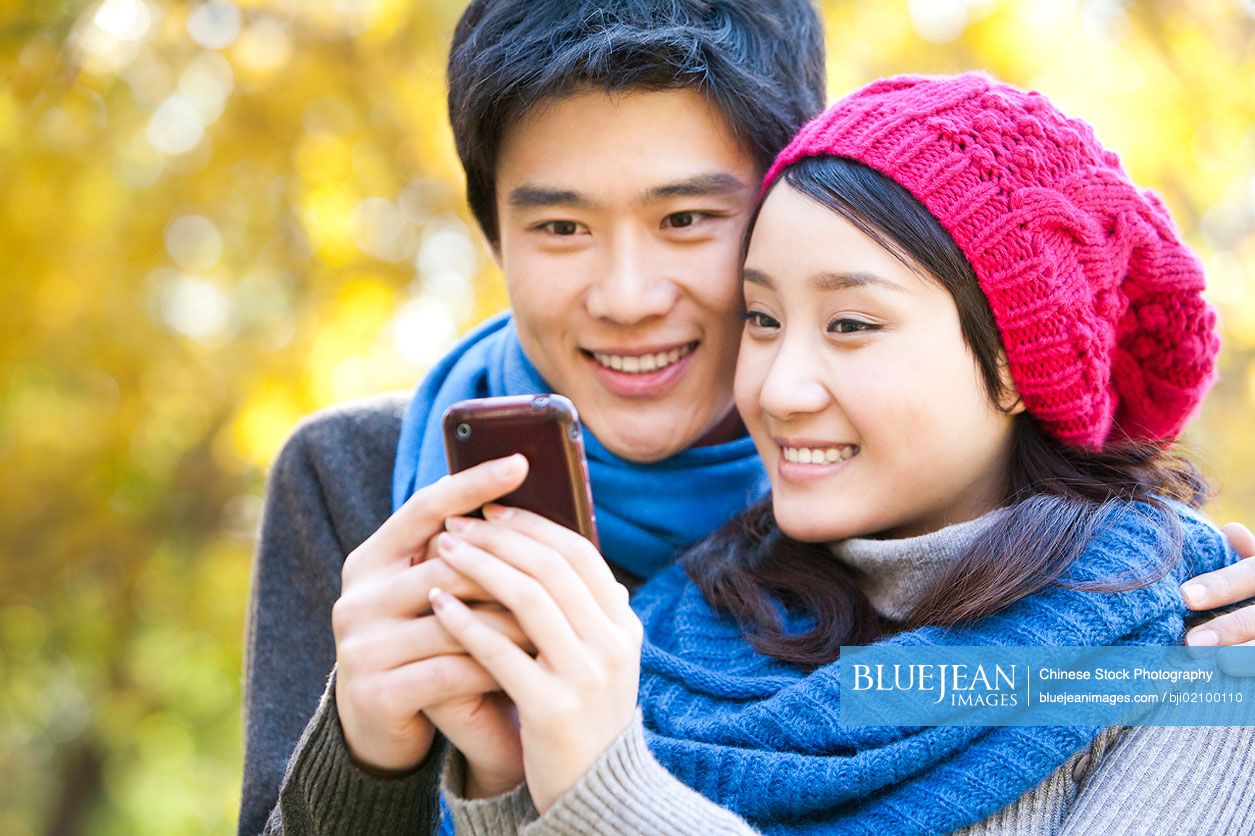 Young Chinese woman showing smart phone to young man