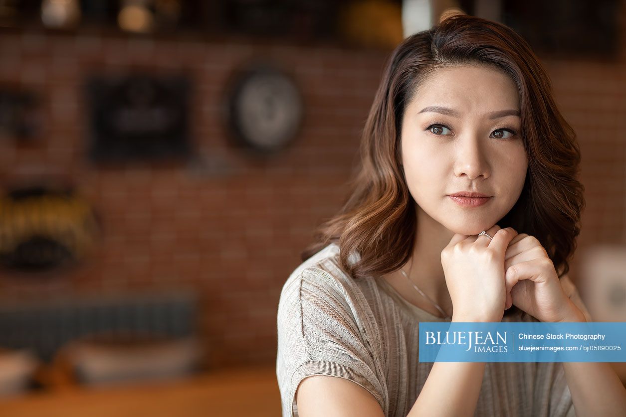 Elegant Chinese woman with hand on chin in cafe