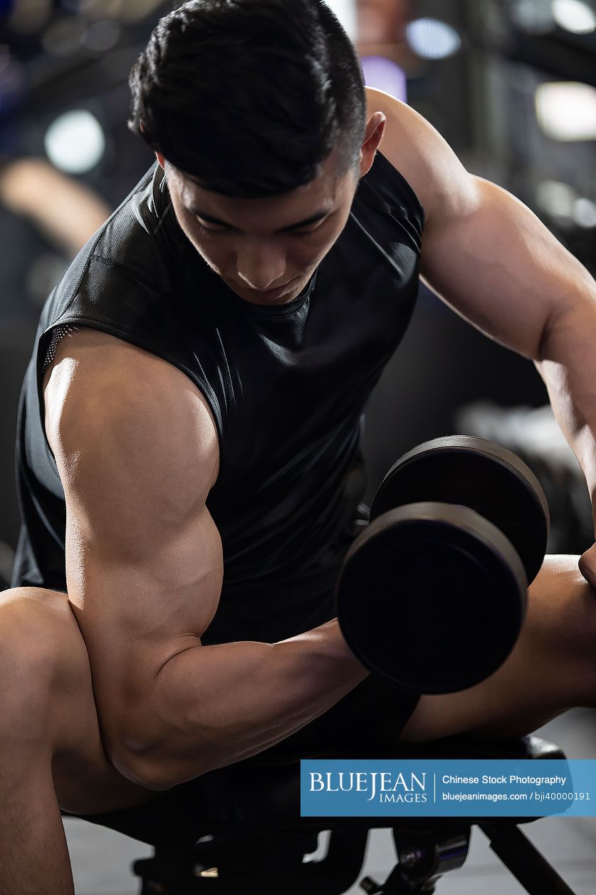 Young Chinese man working out with dumbbell at gym