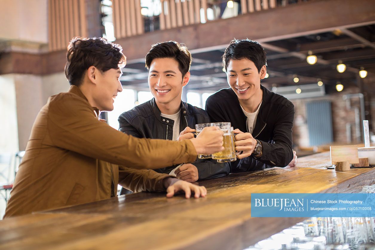 Happy young Chinese men toasting in bar