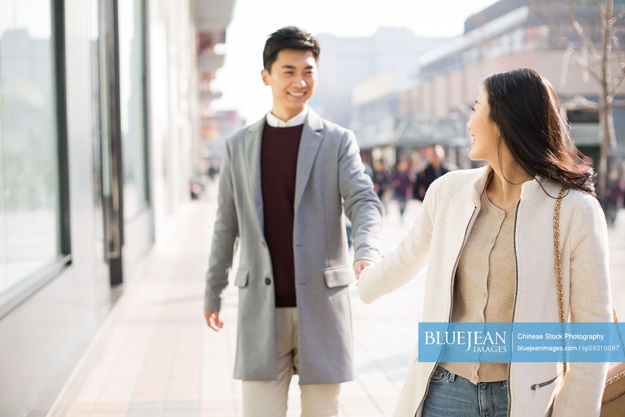 Cheerful young Chinese couple holding hands walking