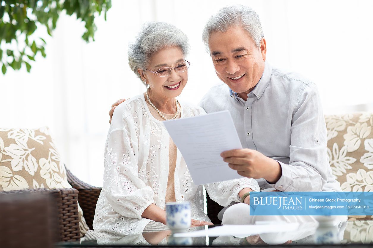 happy-senior-chinese-couple-reading-file-in-living-room-high-res-stock