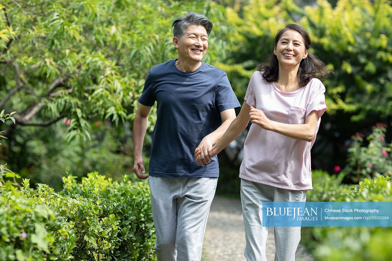 Happy mature Chinese couple running in park