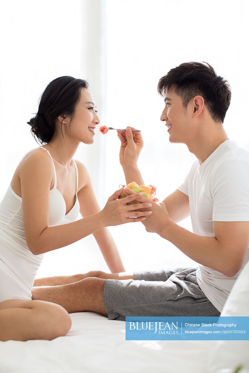 Happy young couple eating fruit salad on bed