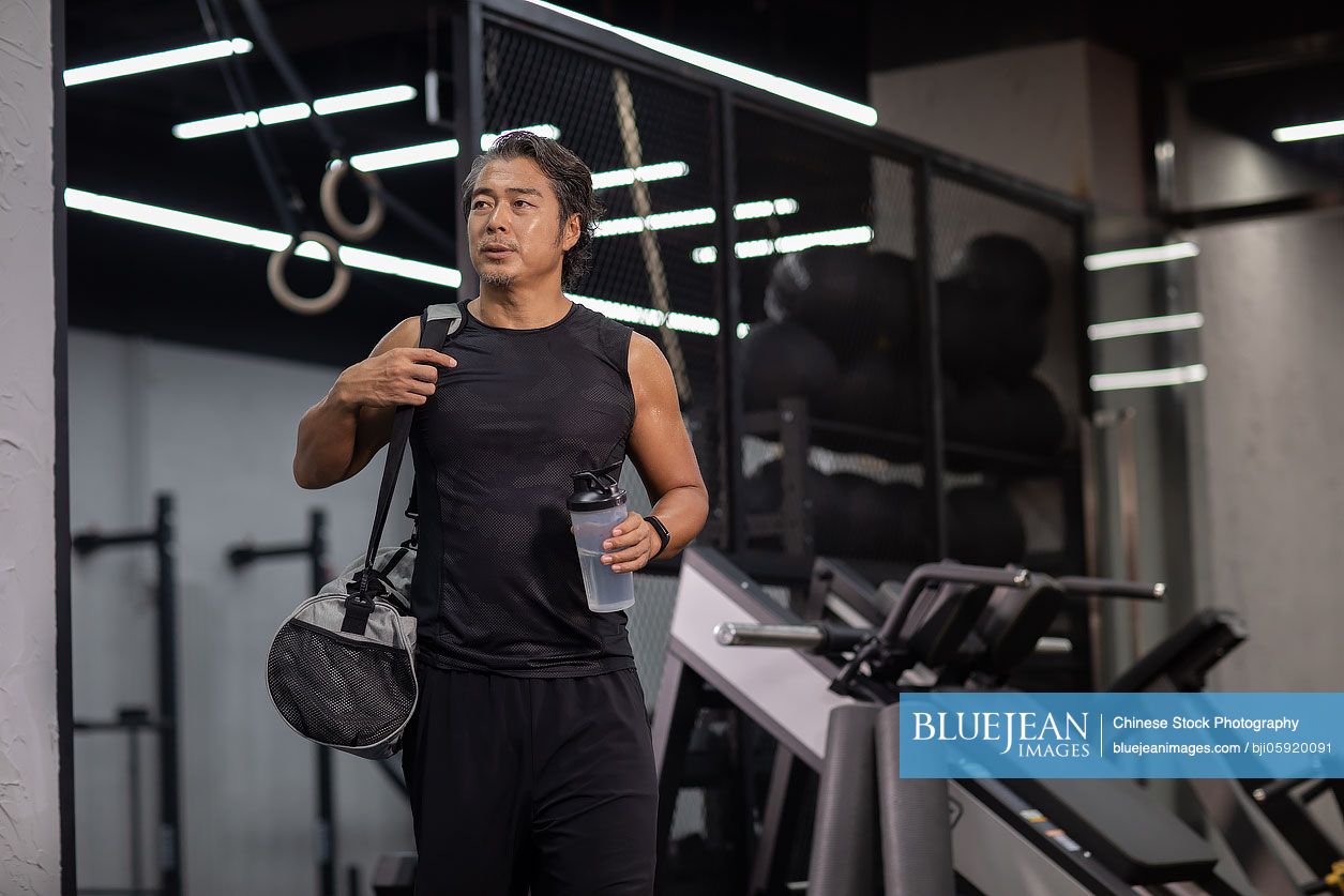 Mature Chinese man with gym bag at gym