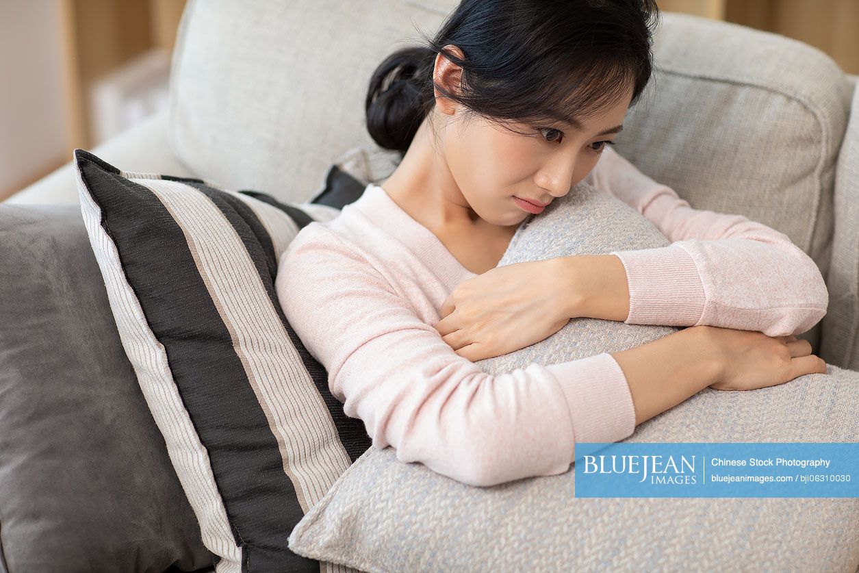 Unhappy young Chinese woman on sofa