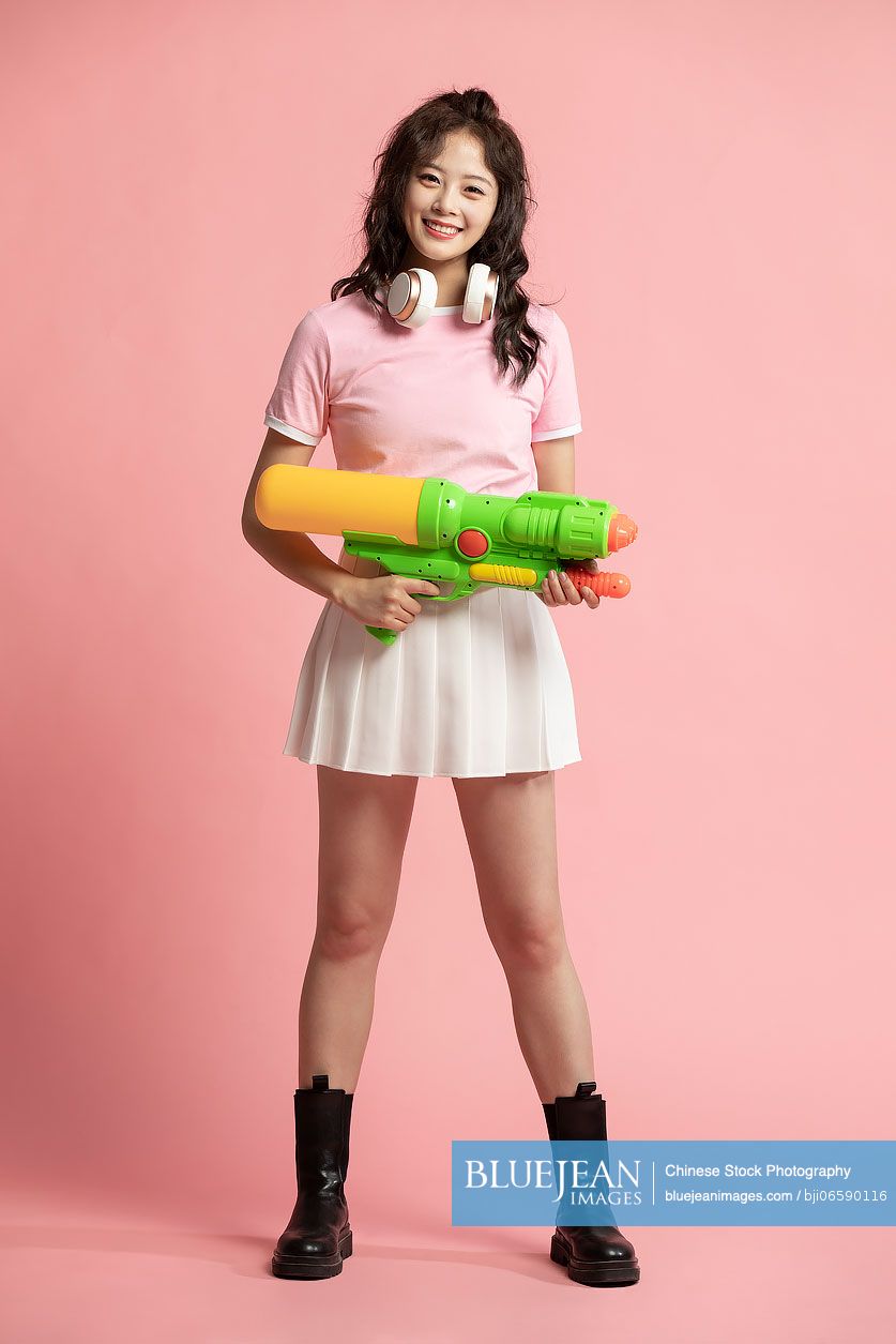 Studio shot of cute young Chinese woman holding a squirt gun