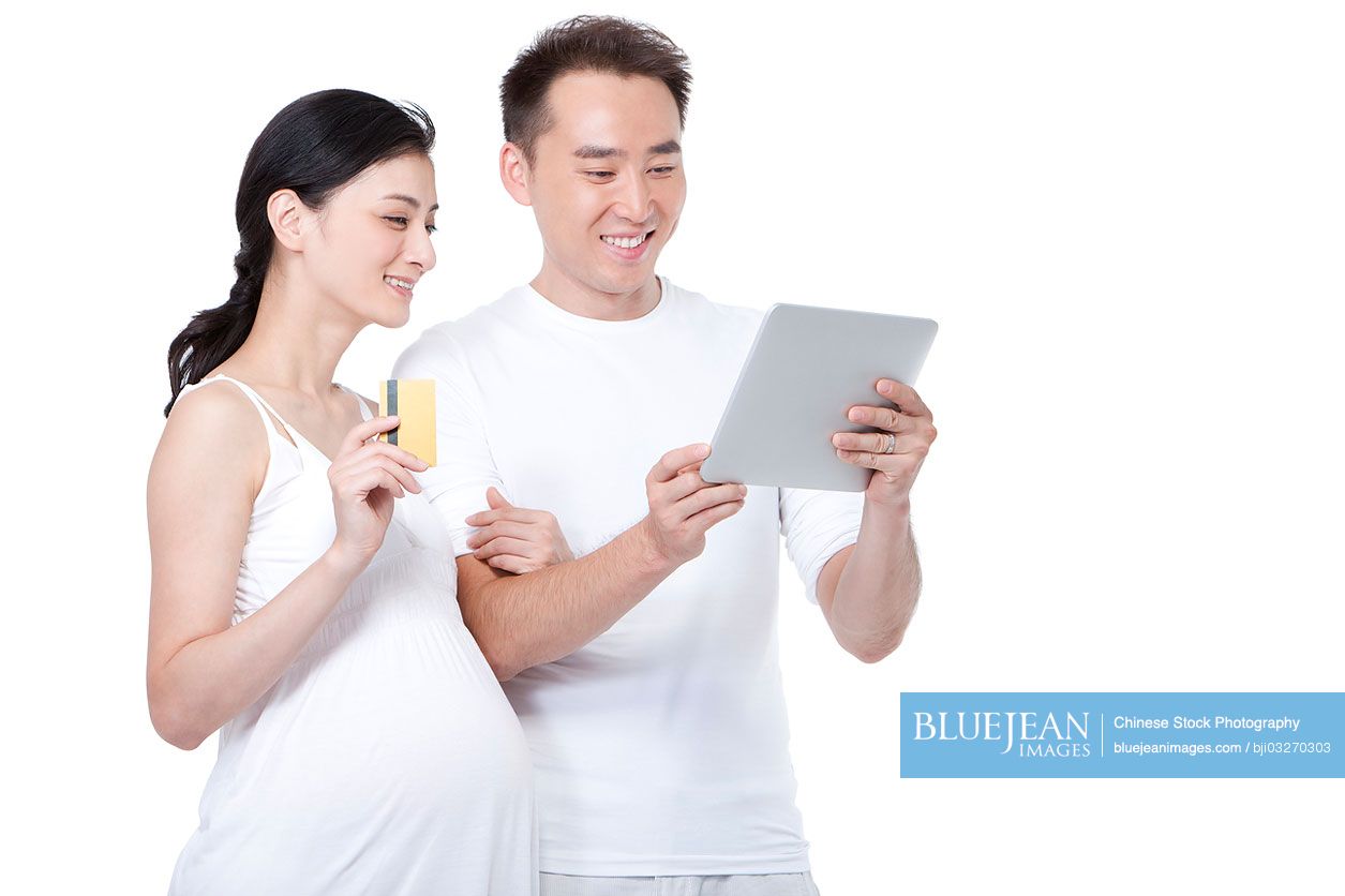 Chinese pregnant woman and man with credit card and digital tablet