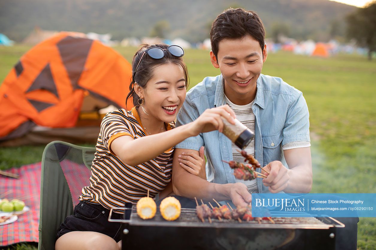 Happy young Chinese couple barbecuing outdoors