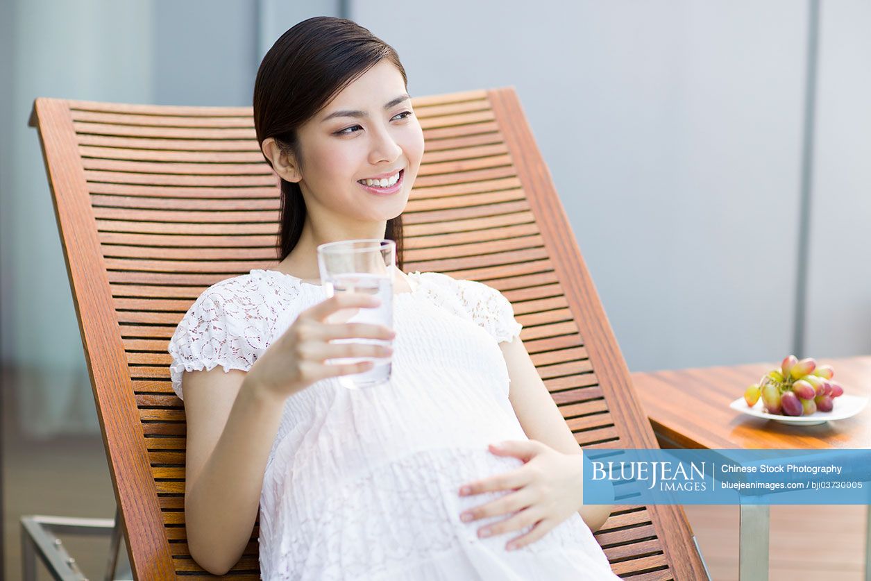 Pregnant Chinese woman drinking water on chaise  longue
