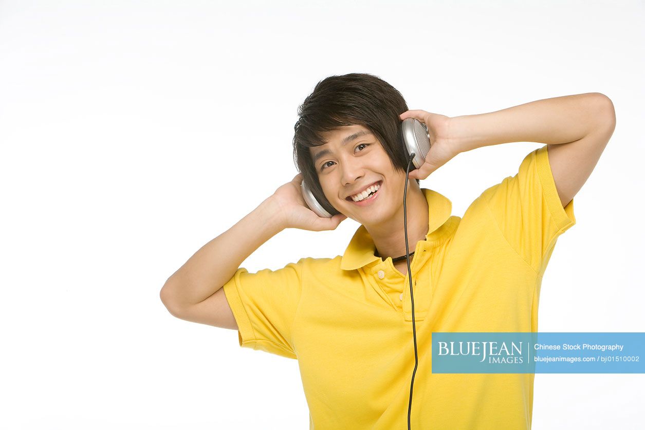 Smiling young Chinese man listening to music on headphones