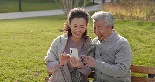 Cheerful senior Chinese couple using smart phone in the park,4K