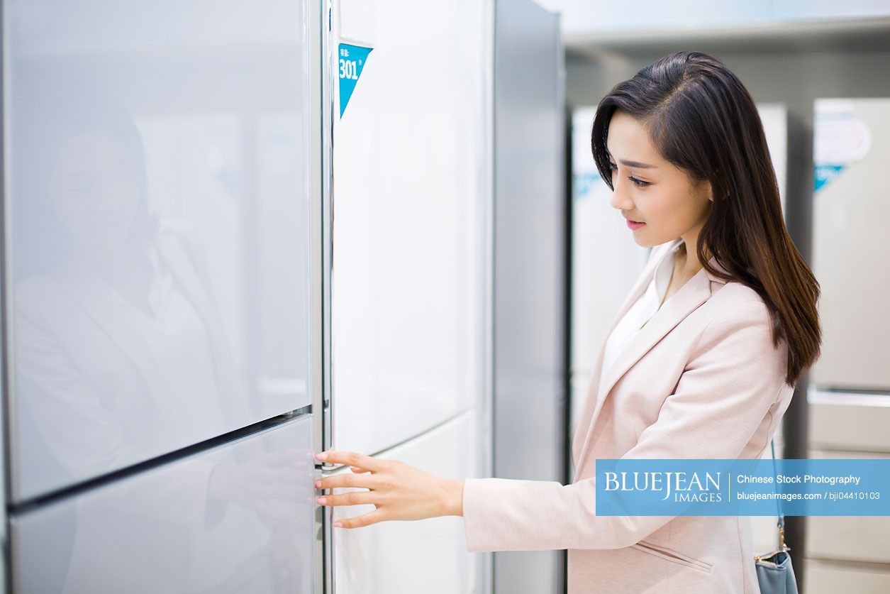 Young Chinese woman buying refrigerator in electronics store