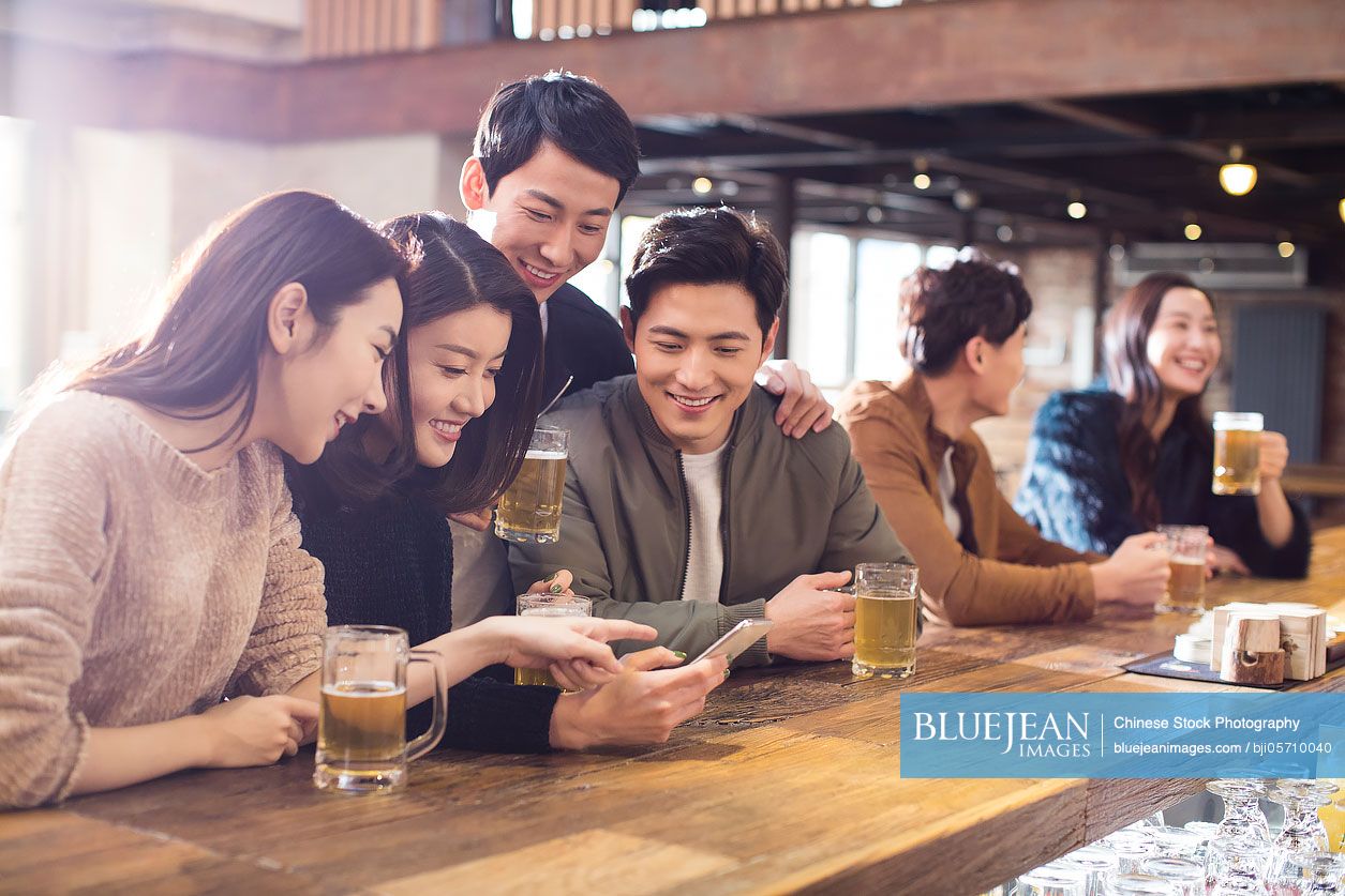 Happy Chinese friends using smartphone in bar