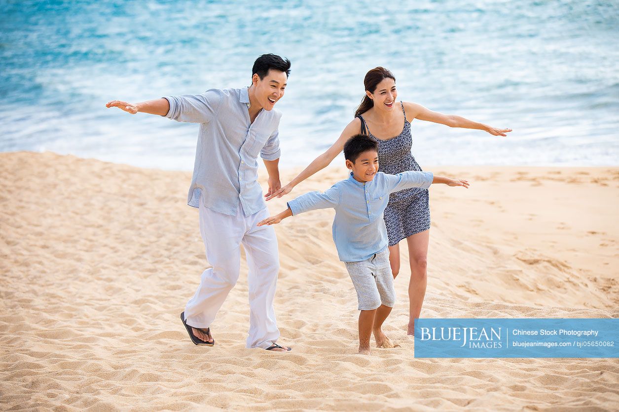 Happy young Chinese family pretending to be flying on beach