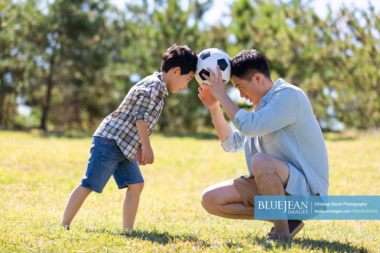 Happy Chinese father and son playing football in park