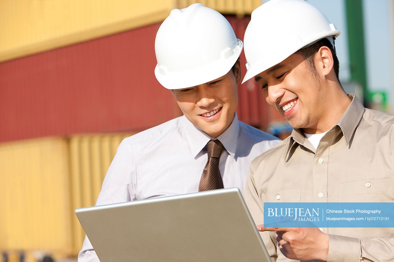 Chinese businessman with shipping industry worker looking over a laptop