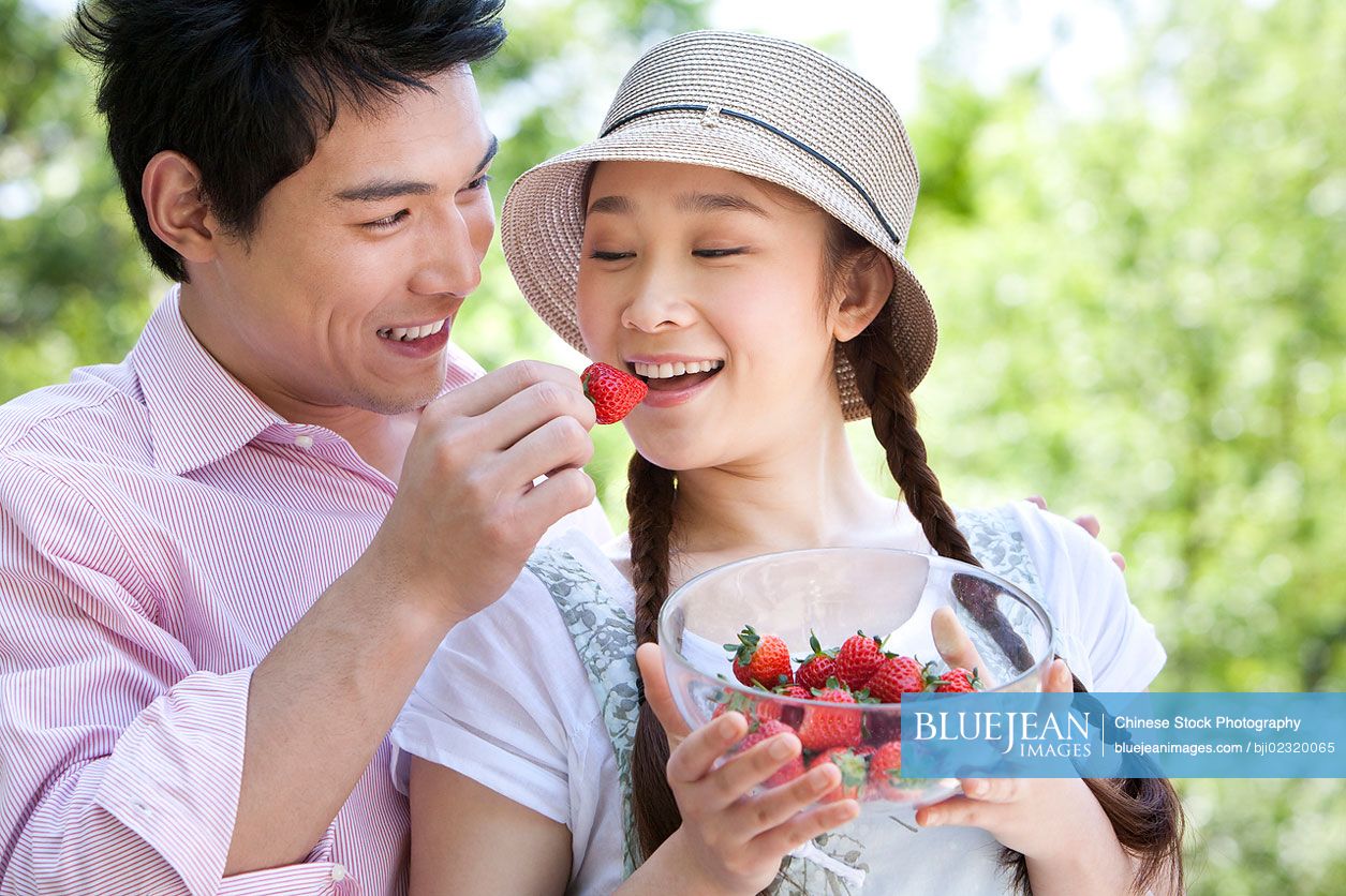 Chinese man feeding woman strawberries in the park
