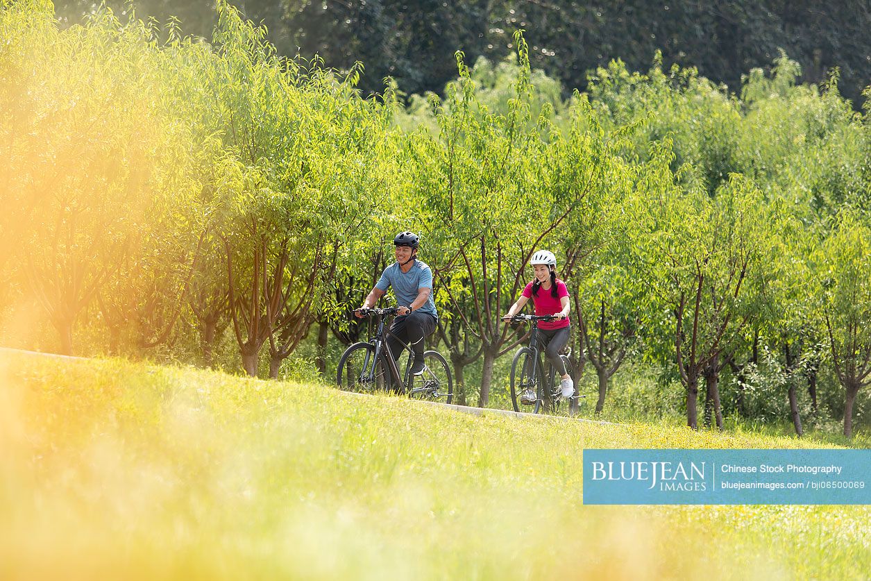 Happy mature Chinese couple riding bikes in park