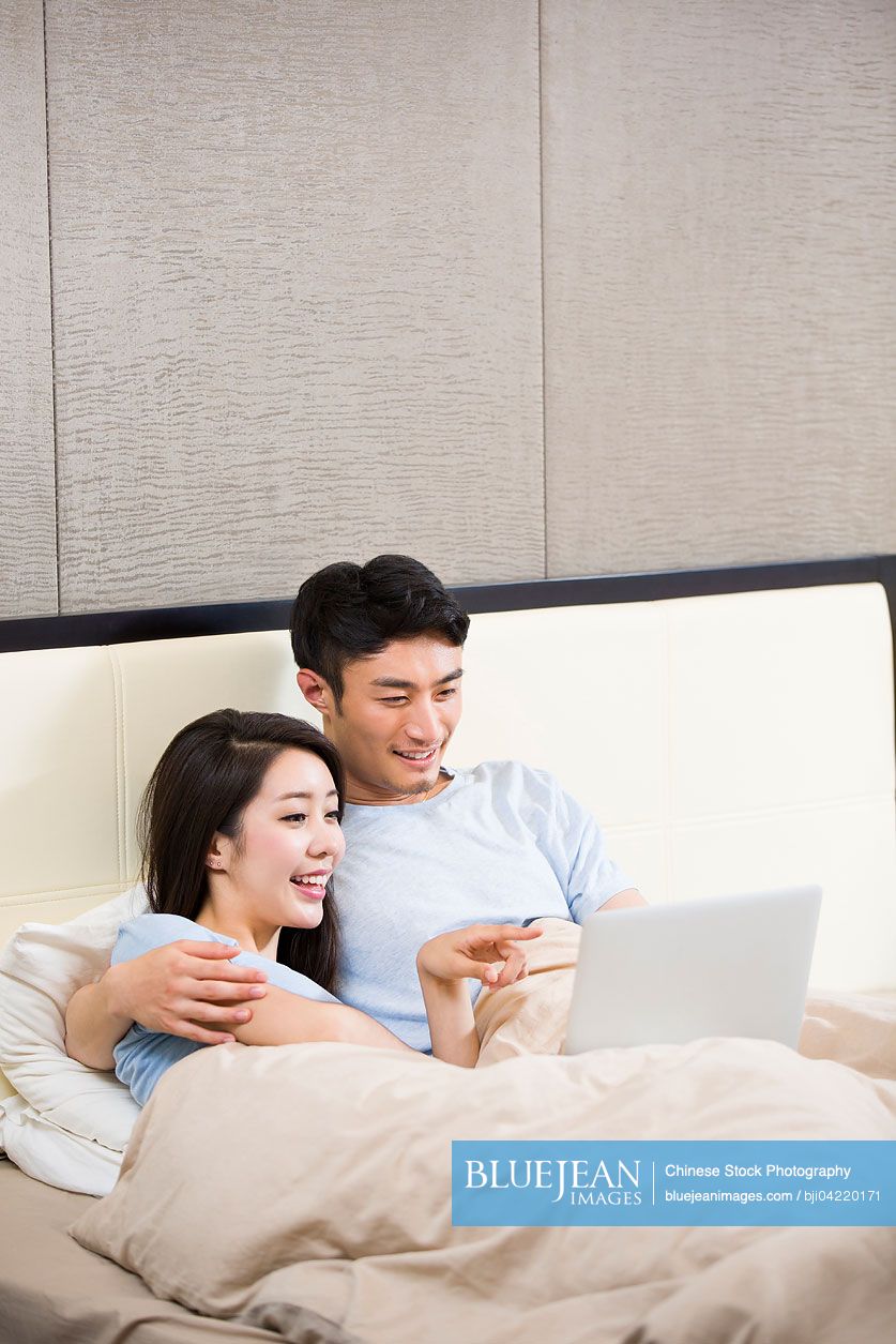 Young Chinese couple using digital tablet on bed
