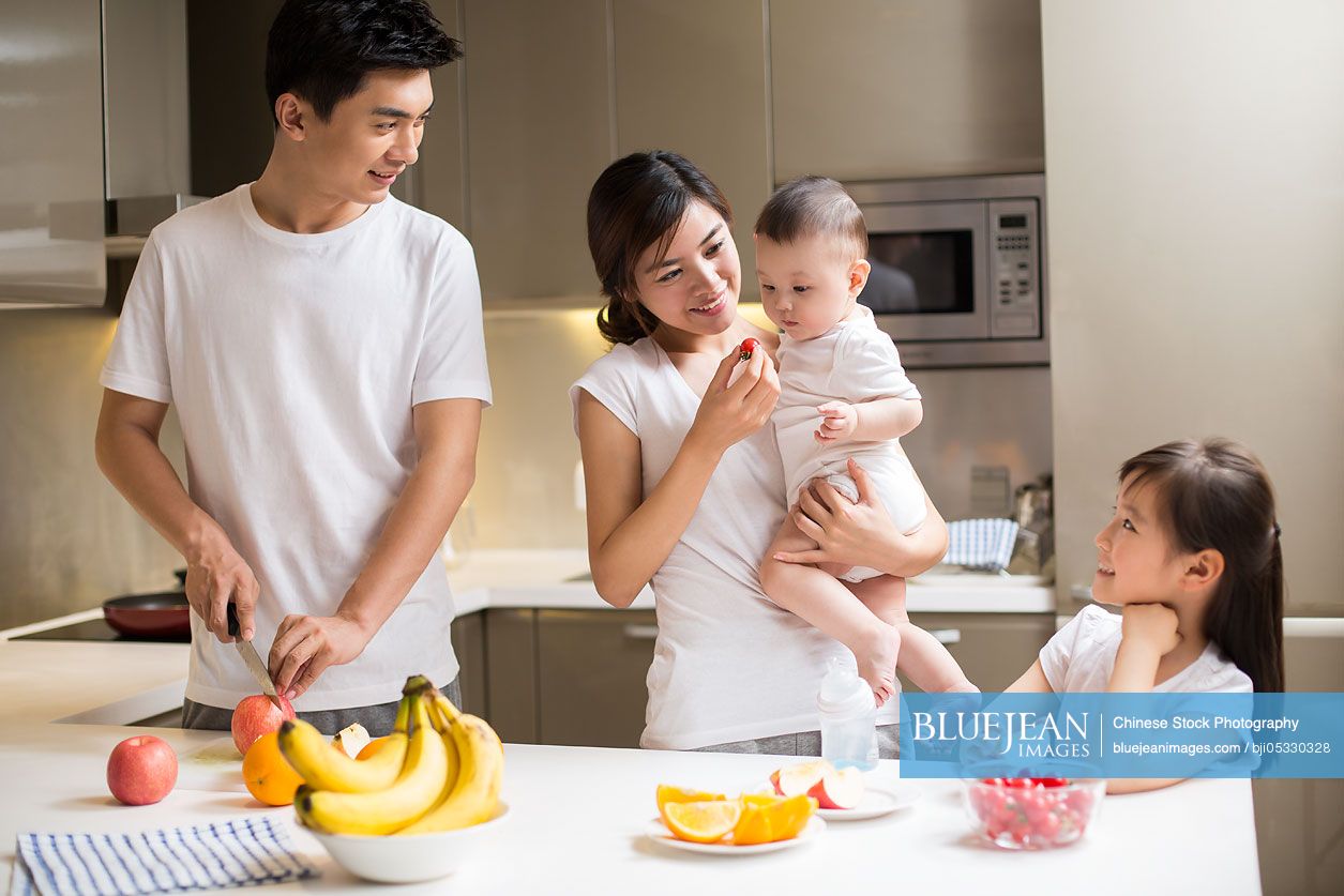 Happy young Chinese family eating fruit in the kitchen